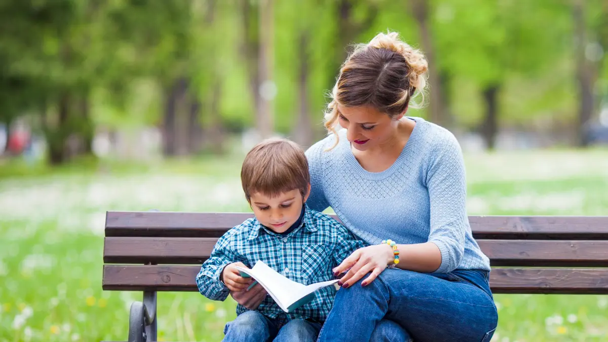 Mamma e figlio leggono libri in inglese per bambini in un parco primaverile.
